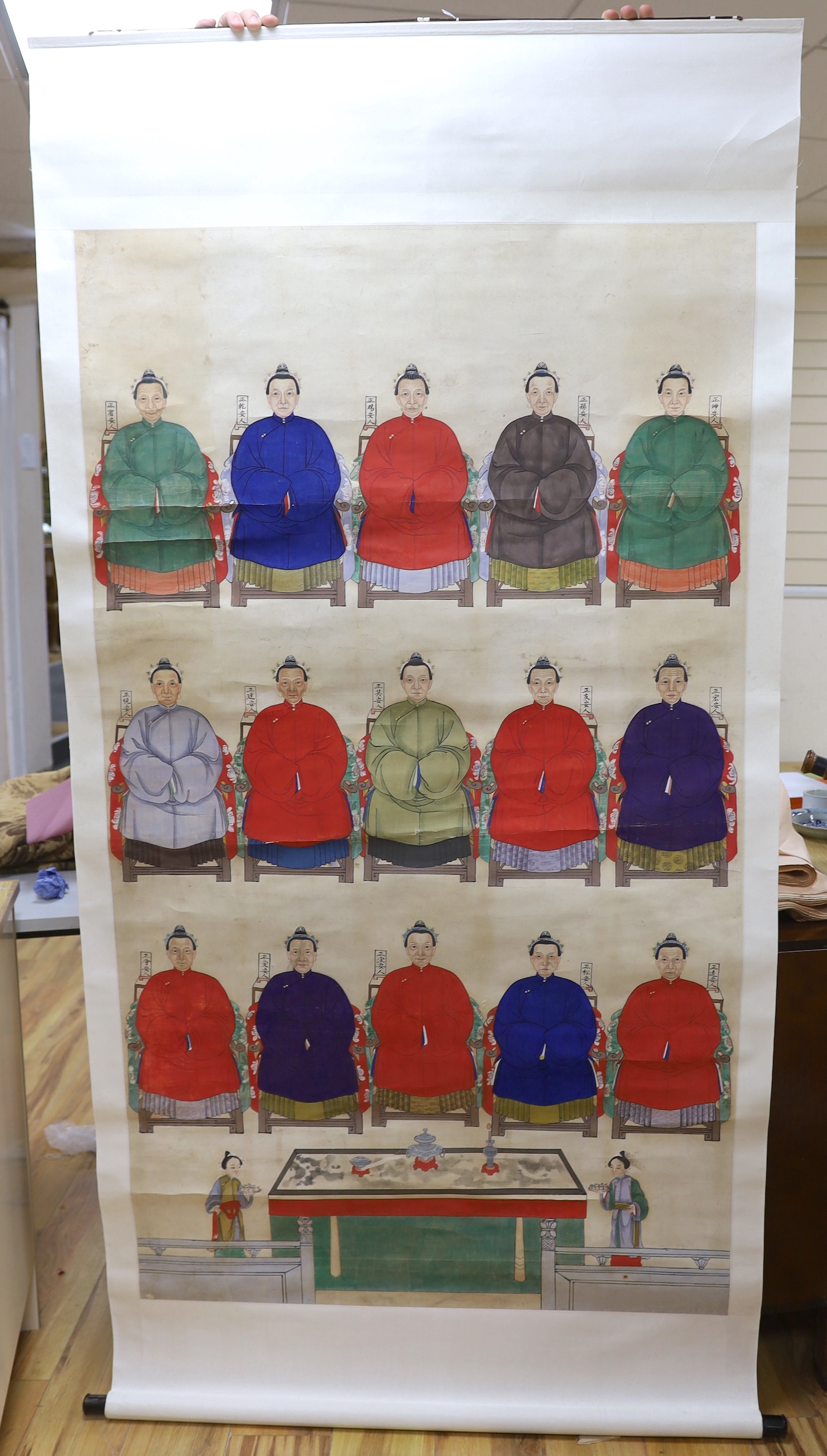 A Chinese ancestor scroll painting on paper, late Qing dynasty, depicting fifteen women seated in formal robes, with two attendants offering gifts below, Image 159cm x 91cm, later mounted